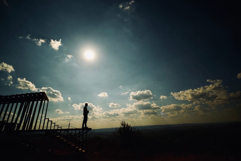 Siluetă de fotograf pe o platformă de lemn, cu soarele deasupra dealurilor