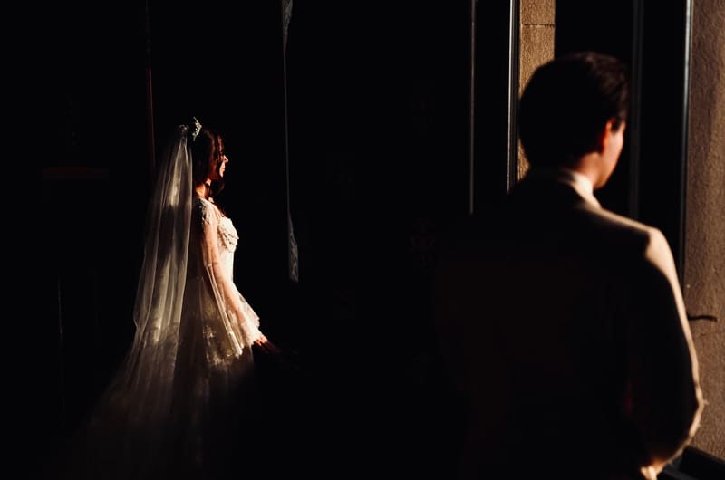 Mireasă luminată de o rază, cu mirele în prim-plan, siluetat
